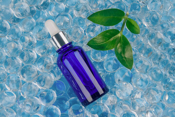 Mockup blue dropper bottle with natural organic herbal cosmetic oil or hyaluronic acid on blue background of water gel balls. Trendy still life composition with copy space. Modern apothecary concept