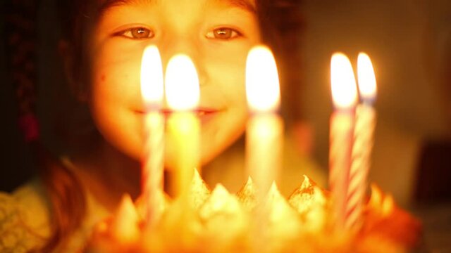 The girl looks at the burning candles on the cake and makes a wish. Birthday, candle flame, orange fire, happy eyes of a child. Children's holiday. Close-up