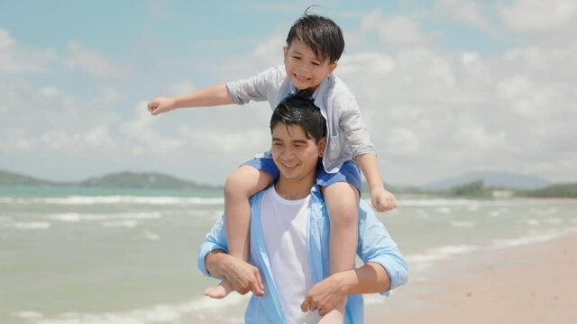 Asian son sitting on his father neck at the beach on the summer day.