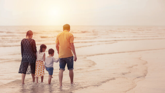 Rear view image of happy asian family dad and mom with their children boy and girl  walking together on sunrise beach during happy day