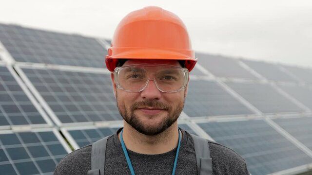 Close up portrait of male electrical worker in protective helmet standing near solar panel. Clean energy production. Green energy. Ecological solar farm.