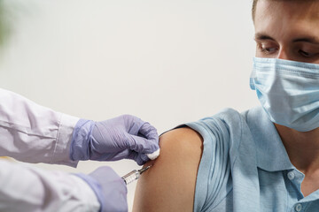 doctor gives an adult young man in a medical mask an injection in the shoulder. Vaccination of adults against coronavirus. vaccine against Covid-19. Protection against the virus. Close up. copy space