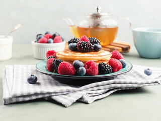 Stack of pancakes with raspberries and blueberries served with green tea