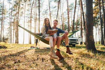 Reading book. Young couple is traveling in the forest at daytime together