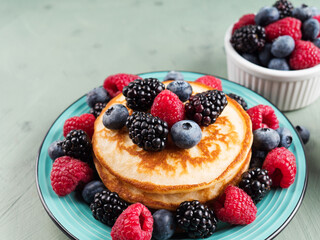 Stack of pancakes with raspberries and blueberries served in a dish on green background