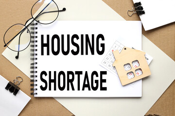 HOUSING SHORTAGE. the text on the notebook on which the wooden figure of the house lies