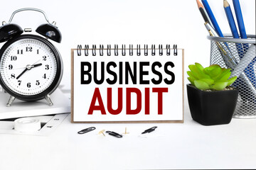 BUSINESS AUDIT. a notebook on a work table, near a desk clock, a flowerpot and a glass with pencils