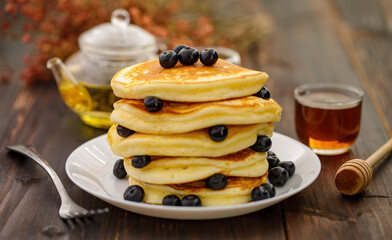 Sweet food. Stack of delicious pancakes with blueberries and honey in white plate on blur wooden background.