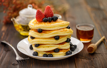 Sweet food. Stack of delicious pancakes with blueberries, Strawberry and honey in white plate on blur wooden background.