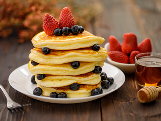 Sweet food. Stack of delicious pancakes with blueberries, Strawberry and honey in white plate on blur wooden background.