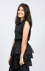 Horizontal portrait shot of a junior young Thai-Turkish teenager in a black dress standing and looking to copy space at the side of the image with raising hand to cheek isolated on white background