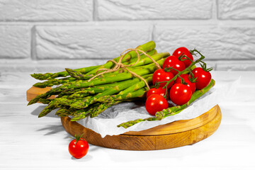 Tomato and Green Asparagus and on wooden board on white brick Background. Healthy eating. Alkaline Food