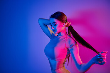 Long brown colored hair. Fashionable young woman standing in the studio with neon light