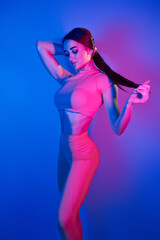 Slim body. Fashionable young woman standing in the studio with neon light