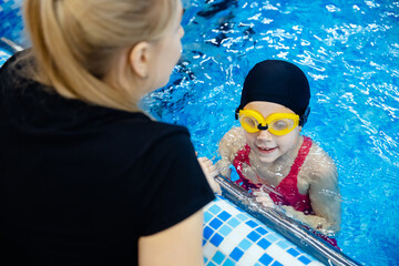 Girl kid learning to swim with women coach at swimming pool