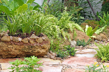 Large container or raised flower bed made of rock by a path in a tropical garden, no people,...