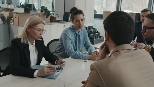 Slowmo shot of team of professional male and female lawyers examining legal documents trying to find gap in law sitting together around table in modern office room