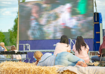 Summer cinema. People and couples watching a movie on the screen of a summer cinema in the evening