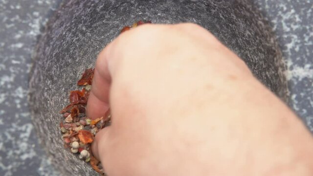 Hand is taking various kinds of spices from the grey stone mortar