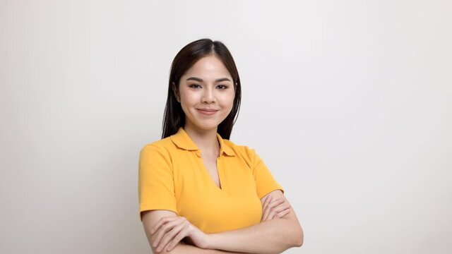 Beautiful young asian woman in yellow shirt smiling and happy. Charming female standing with arms crossed on isolated white background.