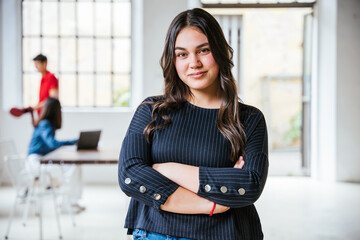 Portrait of a young female businesswoman with arms folded in her new office, behind her two colleagues working together - Successful millennial of a self-confident start-up - Concept of teamwork - 444238888