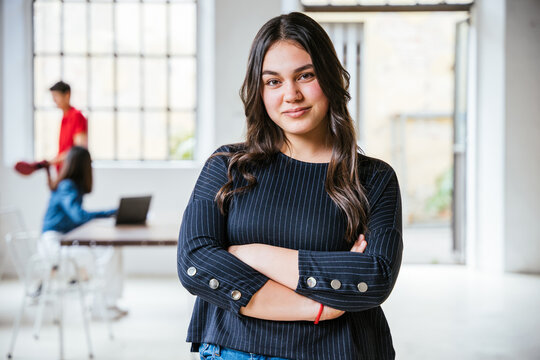 Portrait of a young female businesswoman with arms folded in her new office, behind her two colleagues working together - Successful millennial of a self-confident start-up - Concept of teamwork