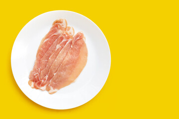 Sliced raw pork meat in white plate on yellow background.