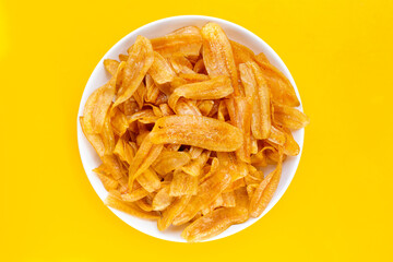 Banana slice chips in white plate on yellow background. © Bowonpat