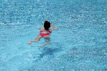Girl in red swimsuit swimming in the pool water. Water sports, beach vacation