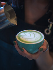 Fototapeta premium A professional barista woman prepares a green matcha tea latte. Latte art close-up, pouring milk into a cup