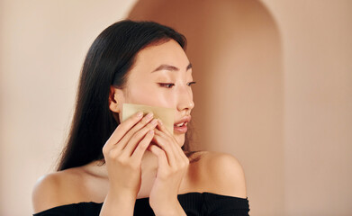 Clearing skin from make up. Young serious asian woman standing indoors