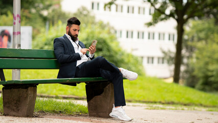 Obraz premium Young businessman sitting on a bench using his cell phone