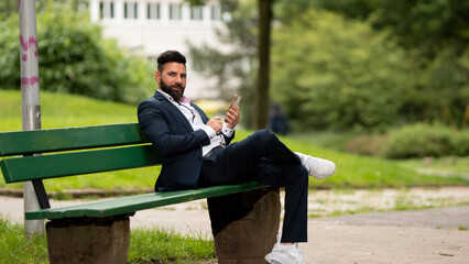 Young businessman sitting on a bench using his cell phone