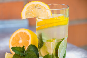 Cool freshly made lemonade in glass on white table. Lemonade with lemon, lime and ice cubes in glass. 