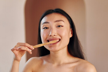 Holds toothbrush. Young serious asian woman standing indoors