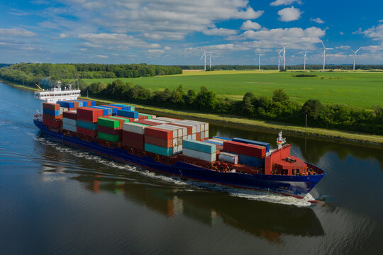 Container ship on the Kiel Canal and windmill on the background.
