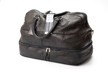 Naklejka premium A black leather, suitcase, travel bag with a faux airline baggage check tag.