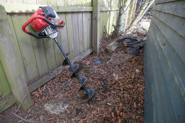 Drill like excavation hole digger power tool leaning against a fence waiting to be used to dig fence post holes