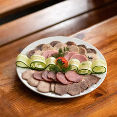 Platter with cold cuts, thin slices of meat, ham and cucumber rolls on wooden table. Soft focus. Copy space.
