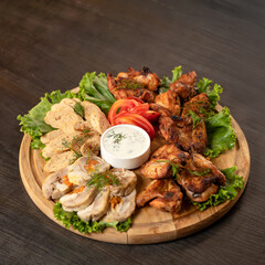 Meat appetizer. Pieces of baked meat and friesh lettuce leaves on wooden cutting board with mayonnaise sauce in center of it. Copy space. Soft focus.