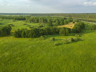 Drone view of a beautiful landscape of a green field with trees and part of the river on a sunny summer day