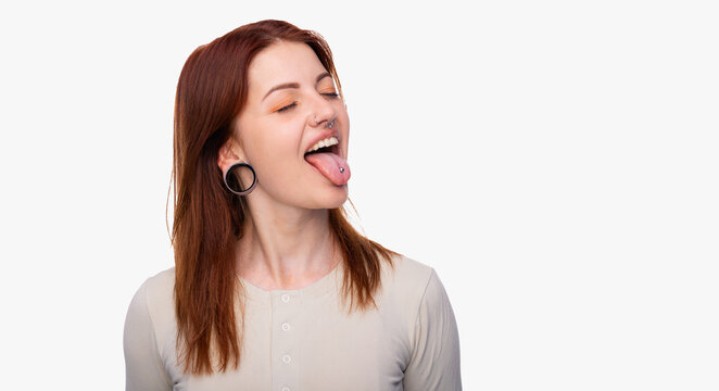 Emotions woman showing tongue. Having earrings in the nose sticking out her tongue and showing piercing. White background, copy space. Woman face piercing