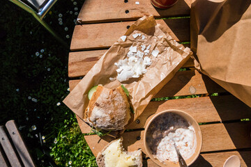 Bread, a cracked hardboiled egg, and a bowl of musli yogurt on a picnic table.
