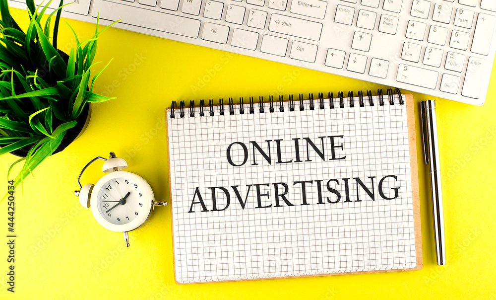 Poster online advertising text on notebook with keyboard , pen and alarm clock on the yellow background