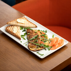 Slices of red fish, omelet with arugula and toast with butter on white platter. Morning mood, breakfast. Soft focus. Copy space.