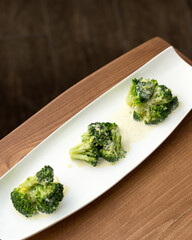 Blanched broccoli with sauce, mini portion. White plate with vegetables on wooden background. Diet...