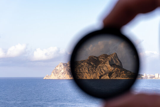 Hand with a neutral density filter for photography demonstrating its operation with a mountain in the background. 