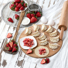 Sweet Dumplings stuffed with strawberries. Slices of raw dough with filling on wooden cutting board. Convenience Food. Cooking process. Top side view. Square format. Soft focus.