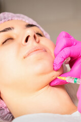 The cosmetologist makes lipolytic injection on the chin of a young woman against the double chin in...