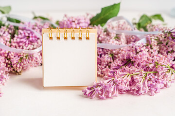 A beautiful floral composition and an empty paper notepad for text. Floral spring background with lilac. Copy space